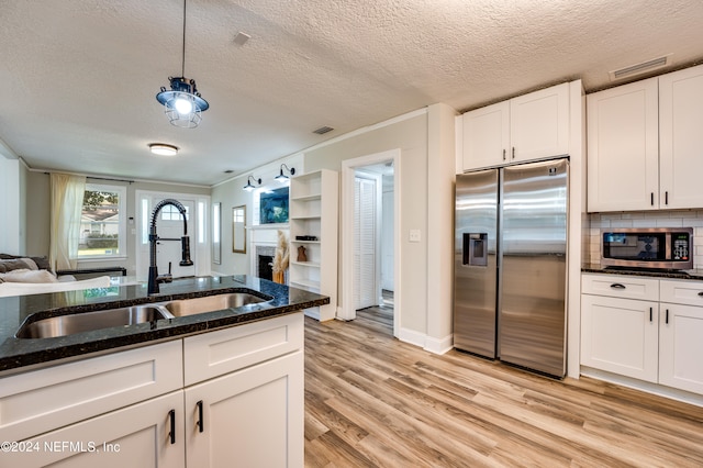 kitchen with dark stone counters, pendant lighting, light hardwood / wood-style floors, white cabinetry, and stainless steel appliances