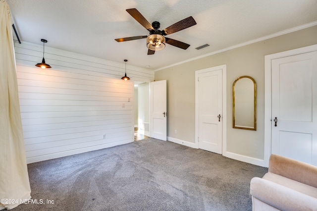 interior space featuring dark colored carpet, a textured ceiling, wooden walls, ornamental molding, and ceiling fan