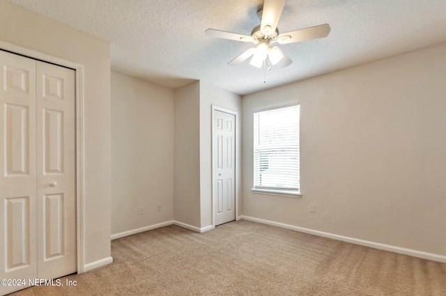 unfurnished bedroom with a textured ceiling, light colored carpet, ceiling fan, and multiple closets