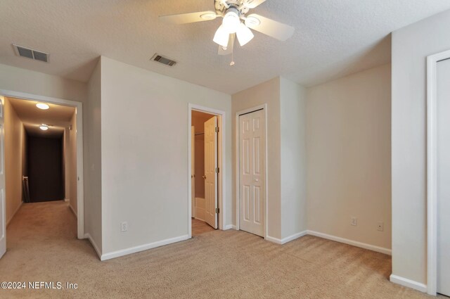 unfurnished bedroom featuring light carpet, ceiling fan, and a textured ceiling