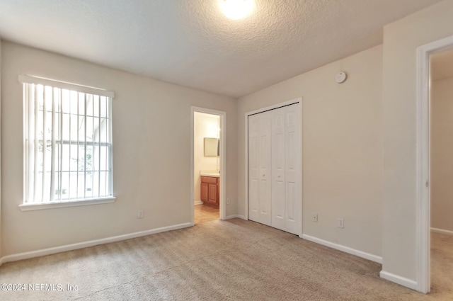 unfurnished bedroom featuring light colored carpet, a textured ceiling, and connected bathroom