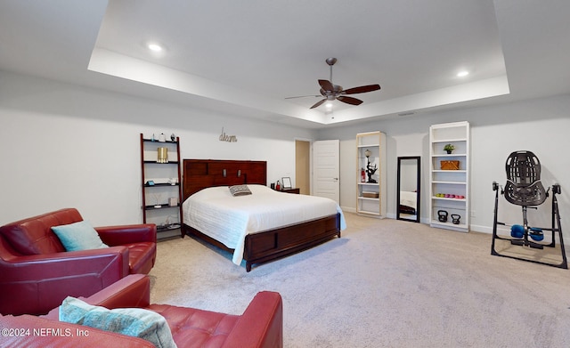 bedroom with ceiling fan, a tray ceiling, and light carpet