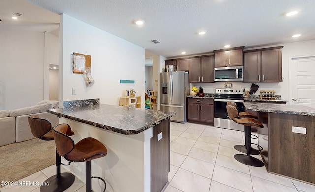 kitchen featuring a textured ceiling, light tile patterned flooring, a breakfast bar area, appliances with stainless steel finishes, and dark brown cabinetry