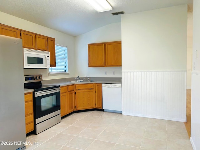 kitchen featuring vaulted ceiling, appliances with stainless steel finishes, sink, light tile patterned floors, and a textured ceiling