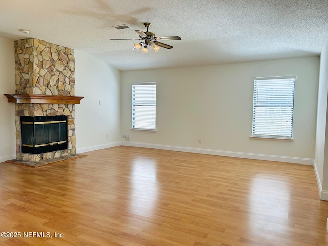 unfurnished living room featuring light wood-style flooring, a ceiling fan, a stone fireplace, a textured ceiling, and baseboards