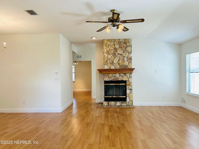 unfurnished living room with ceiling fan, a fireplace, a textured ceiling, and light hardwood / wood-style floors