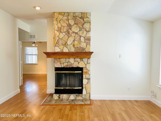 interior details featuring visible vents, a stone fireplace, a textured ceiling, and wood finished floors