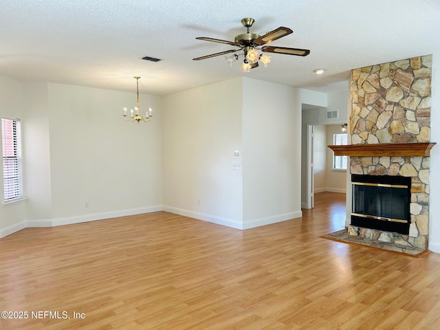 unfurnished living room featuring light wood finished floors, visible vents, a textured ceiling, and a stone fireplace