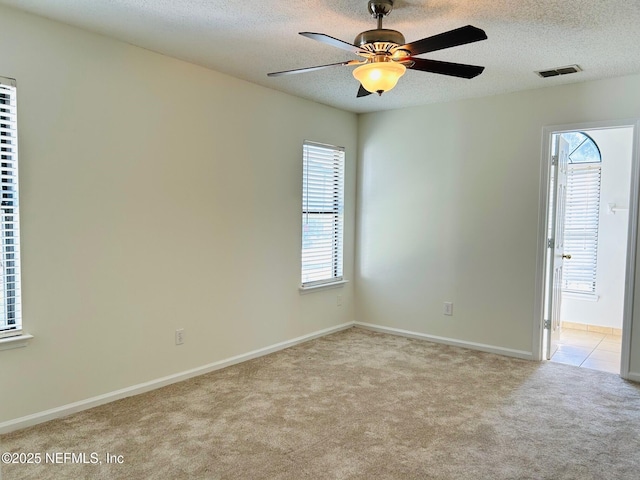 spare room with a textured ceiling, ceiling fan, light colored carpet, visible vents, and baseboards