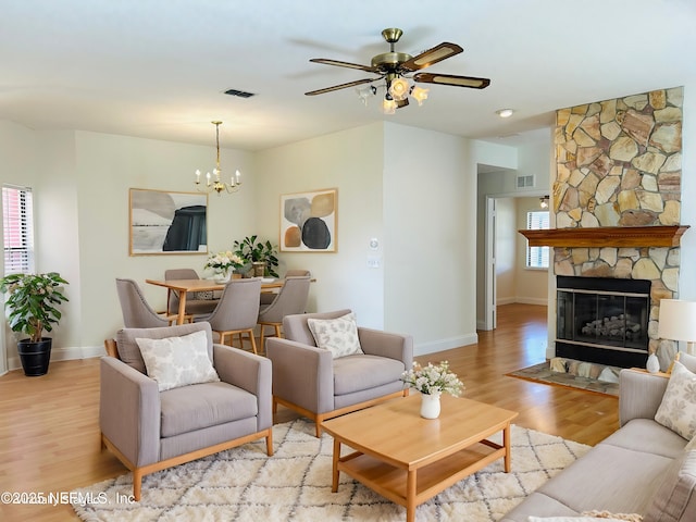 living room featuring ceiling fan with notable chandelier, a fireplace, and light hardwood / wood-style floors