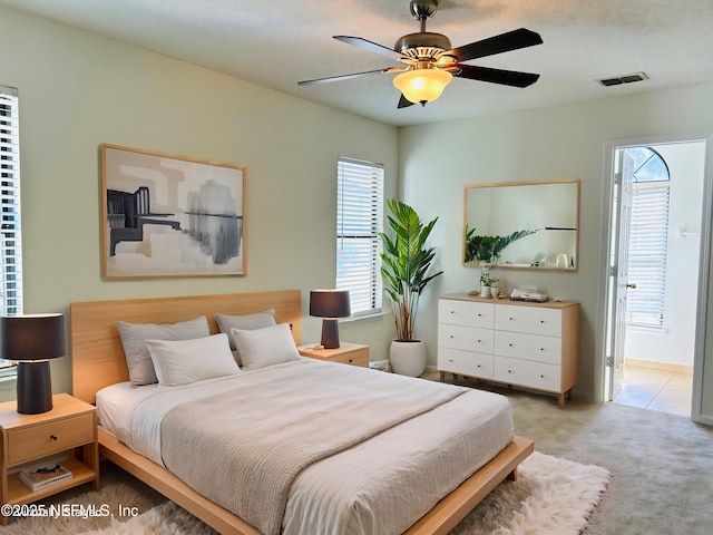 bedroom featuring a ceiling fan, visible vents, connected bathroom, and light colored carpet