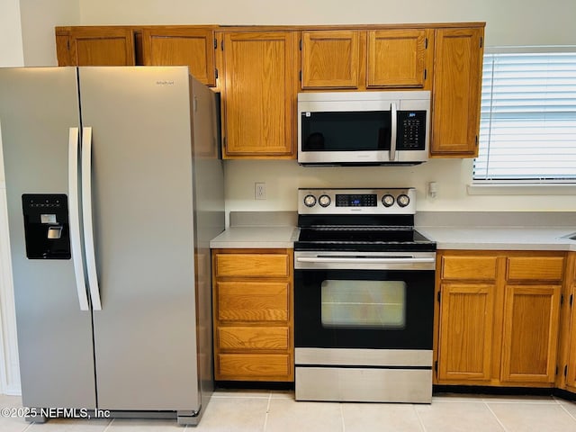 kitchen featuring light countertops, appliances with stainless steel finishes, brown cabinetry, and light tile patterned flooring