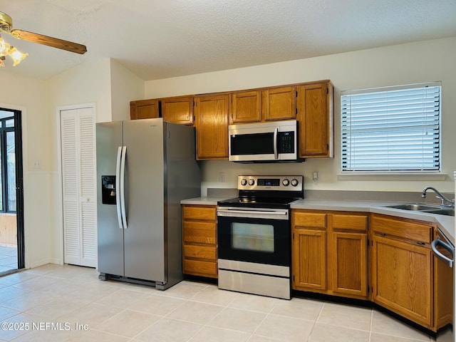 kitchen with light tile patterned floors, appliances with stainless steel finishes, brown cabinets, light countertops, and a sink