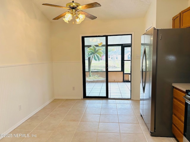 interior space featuring light tile patterned floors, ceiling fan, a textured ceiling, and wainscoting