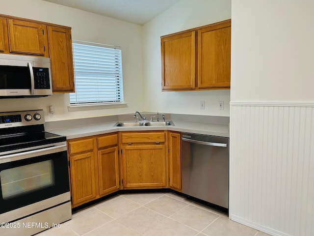 kitchen with light tile patterned floors, stainless steel appliances, a sink, light countertops, and brown cabinetry