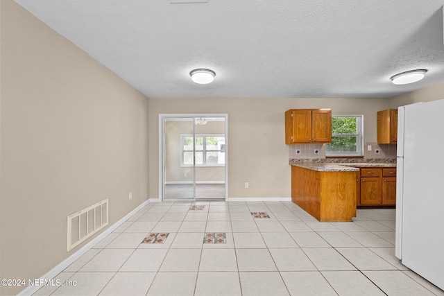 kitchen featuring backsplash, white refrigerator, light tile patterned floors, and a textured ceiling