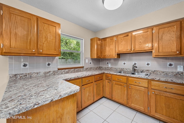 kitchen with light stone counters, a textured ceiling, tasteful backsplash, sink, and light tile patterned floors