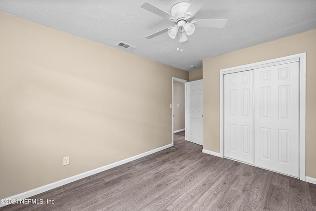 unfurnished bedroom with a textured ceiling, hardwood / wood-style floors, ceiling fan, and a closet