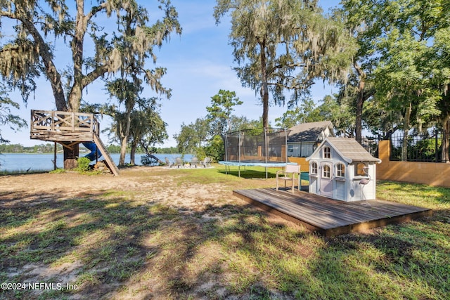 view of yard with a deck with water view, a trampoline, and an outbuilding