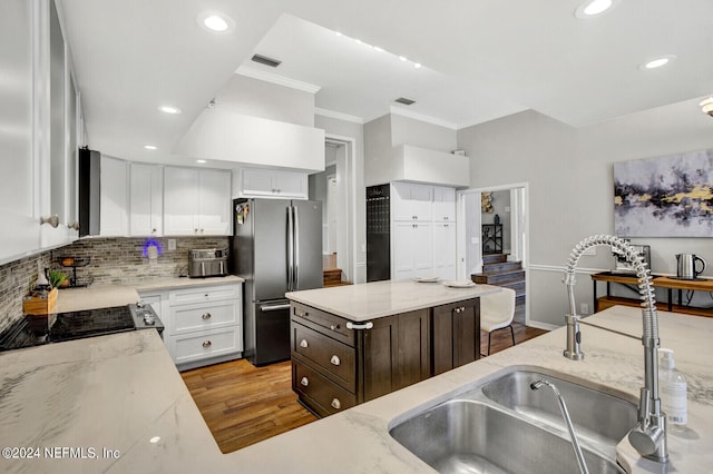 kitchen with light stone countertops, stainless steel refrigerator, sink, and white cabinets