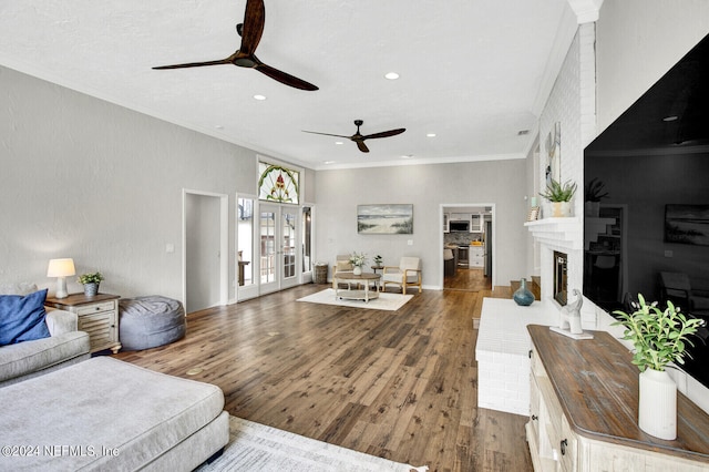 living room featuring a fireplace, french doors, dark hardwood / wood-style flooring, ceiling fan, and crown molding