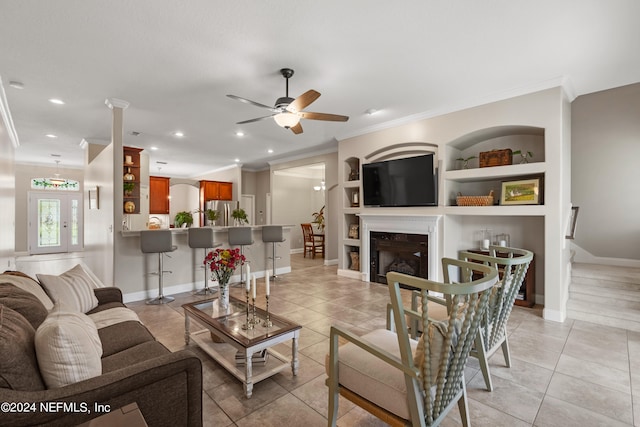 tiled living room with crown molding, ceiling fan, and built in shelves