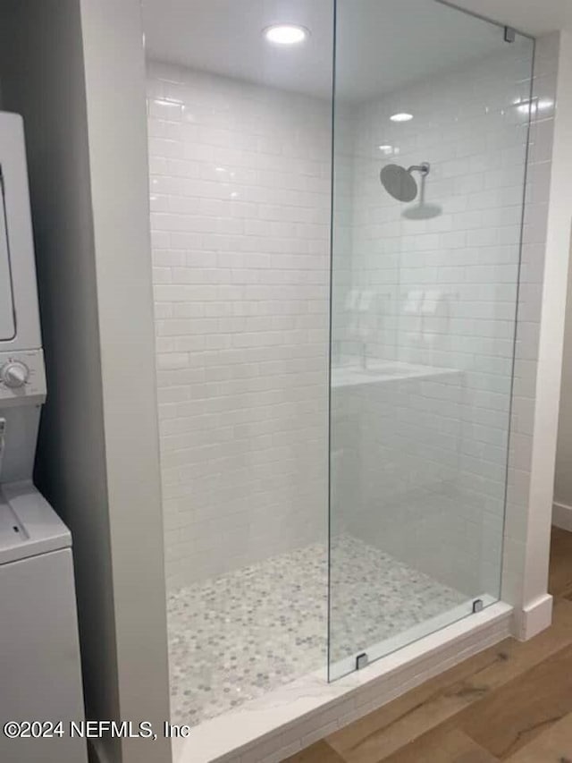 bathroom with tiled shower, stacked washer and dryer, and hardwood / wood-style floors