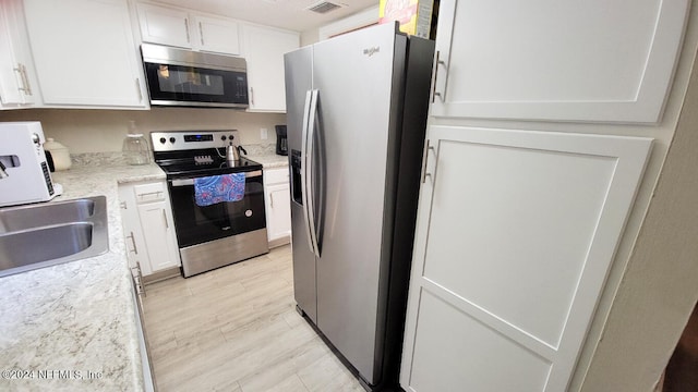 kitchen featuring light wood-type flooring, light stone counters, sink, white cabinets, and appliances with stainless steel finishes