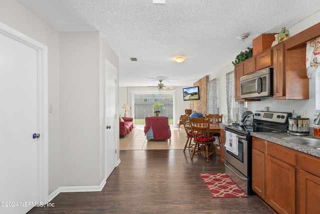 kitchen with appliances with stainless steel finishes, sink, a textured ceiling, ceiling fan, and dark wood-type flooring