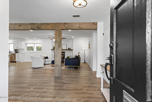 foyer featuring a brick fireplace, beam ceiling, wood-type flooring, and ceiling fan