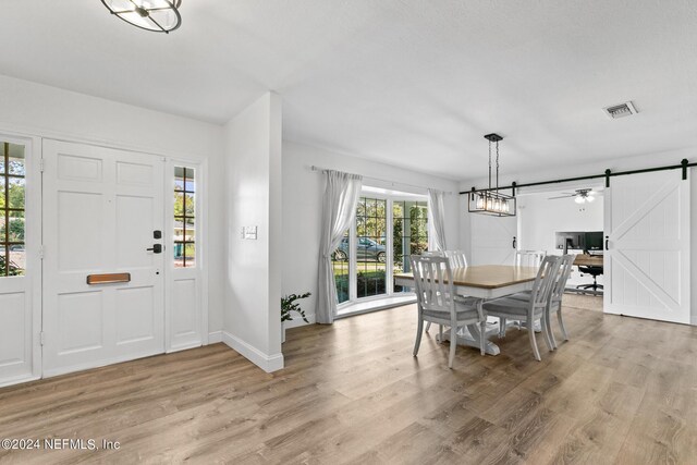 dining space with a barn door, light wood-type flooring, and a chandelier