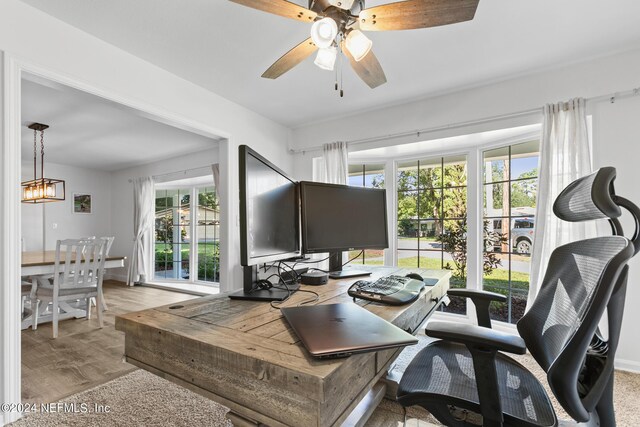 home office with ceiling fan with notable chandelier, light hardwood / wood-style flooring, and a healthy amount of sunlight