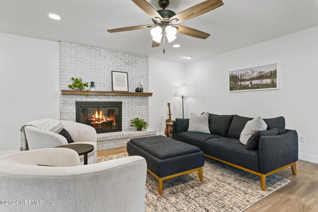 living room with a brick fireplace, ceiling fan, light wood-type flooring, and a textured ceiling