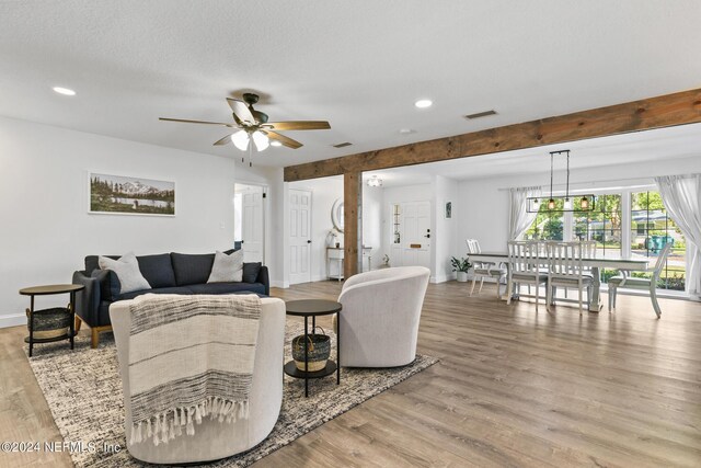 living room with light wood-type flooring, beam ceiling, ceiling fan, and a textured ceiling