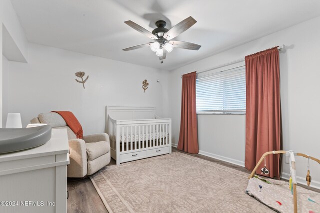 bedroom featuring light hardwood / wood-style floors, a crib, and ceiling fan