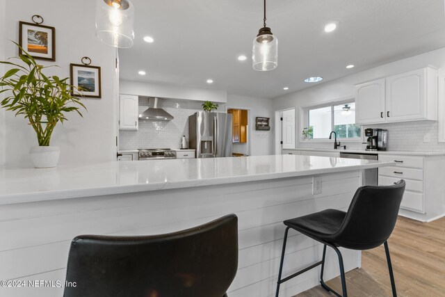 kitchen with light wood-type flooring, tasteful backsplash, white cabinets, wall chimney exhaust hood, and appliances with stainless steel finishes