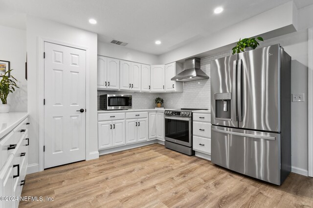 kitchen featuring white cabinets, stainless steel appliances, wall chimney range hood, and light hardwood / wood-style flooring