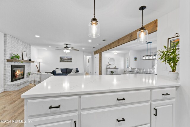 kitchen with white cabinets, a fireplace, light hardwood / wood-style flooring, decorative light fixtures, and ceiling fan