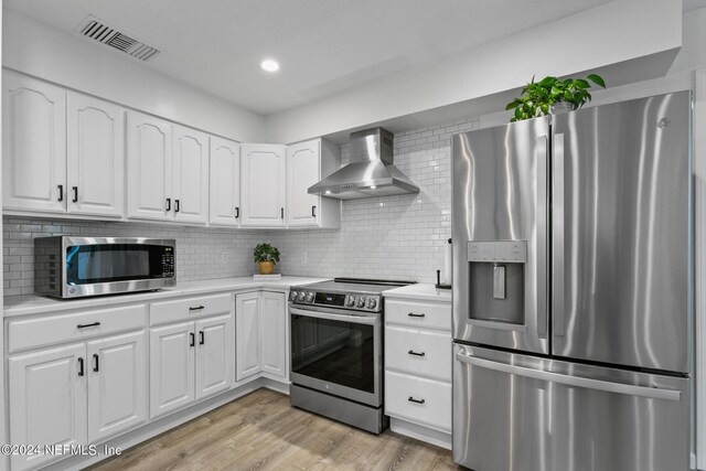 kitchen featuring wall chimney exhaust hood, stainless steel appliances, white cabinetry, and light hardwood / wood-style floors