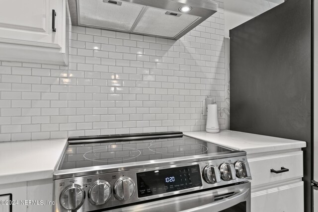 kitchen featuring ventilation hood, backsplash, white cabinetry, and stainless steel range with electric cooktop