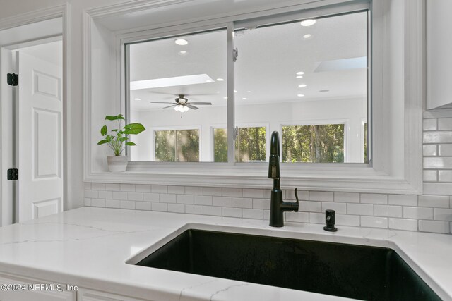 kitchen featuring backsplash, sink, ceiling fan, and light stone counters