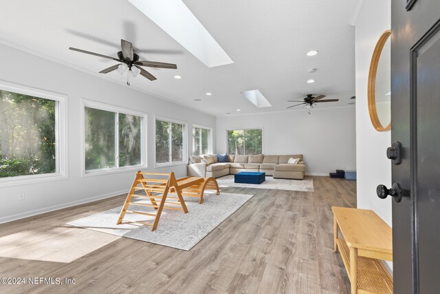 living room featuring light wood-type flooring, a skylight, ceiling fan, and crown molding