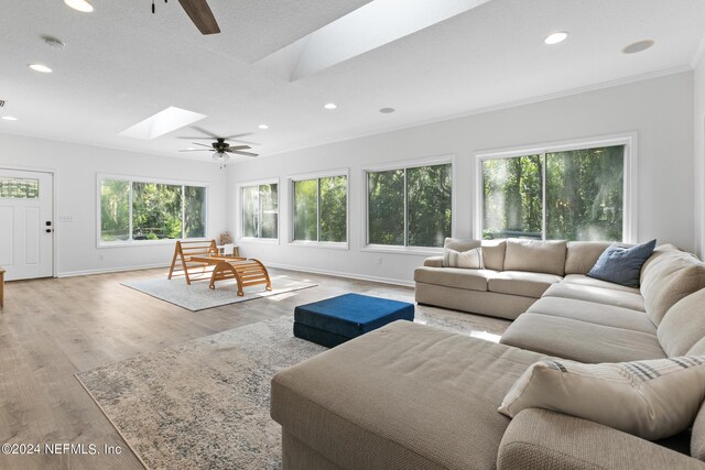 living room with ceiling fan, a skylight, ornamental molding, a textured ceiling, and light wood-type flooring