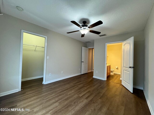 unfurnished bedroom with a closet, a textured ceiling, dark wood-type flooring, a spacious closet, and ceiling fan