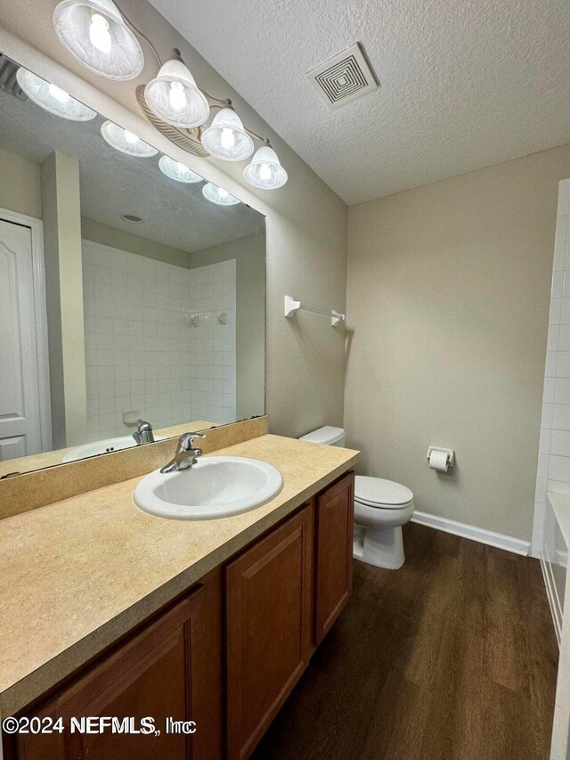 full bathroom with vanity, tiled shower / bath combo, a textured ceiling, hardwood / wood-style flooring, and toilet