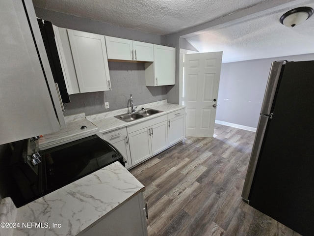 kitchen featuring a textured ceiling, wood-type flooring, white cabinetry, sink, and stainless steel fridge