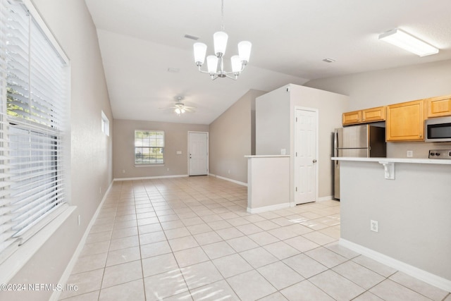 kitchen featuring lofted ceiling, light tile patterned floors, appliances with stainless steel finishes, a kitchen bar, and ceiling fan with notable chandelier