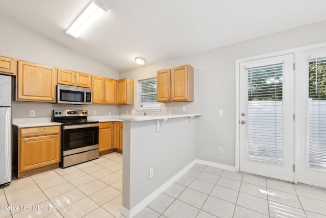 kitchen featuring lofted ceiling, a breakfast bar area, appliances with stainless steel finishes, light brown cabinetry, and light tile patterned flooring