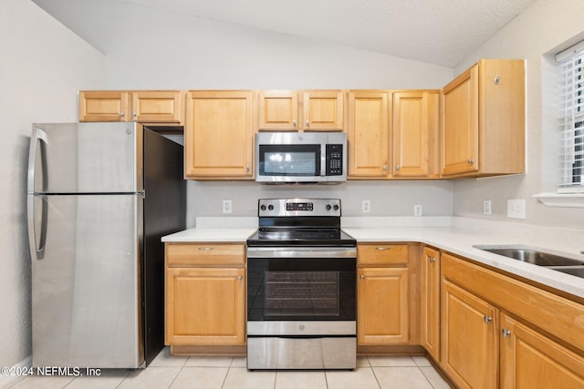 kitchen with light tile patterned floors, stainless steel appliances, lofted ceiling, and light brown cabinets