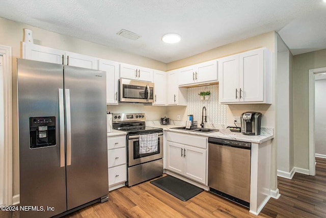 kitchen with a textured ceiling, hardwood / wood-style flooring, sink, white cabinetry, and stainless steel appliances